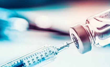 Syringe needle tip going into container of vaccine with blurred background